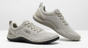 A pair of light grey Xero Shoes with mesh uppers, lace closures, and textured rubber soles. Designed for walking, they offer all-day comfort with ventilation holes and a minimalistic style. The "Xero" brand name is displayed on the shoes.