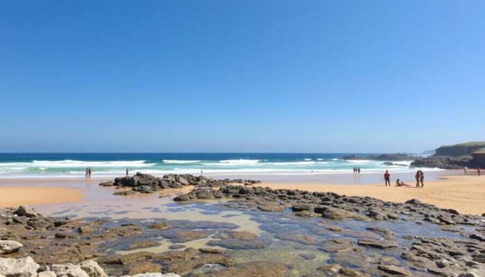 A sunny beach with clear waves and golden sands for sunbathing, rocky outcrops for exploration, accessible ramps, and diverse people enjoying the day under a bright blue sky.